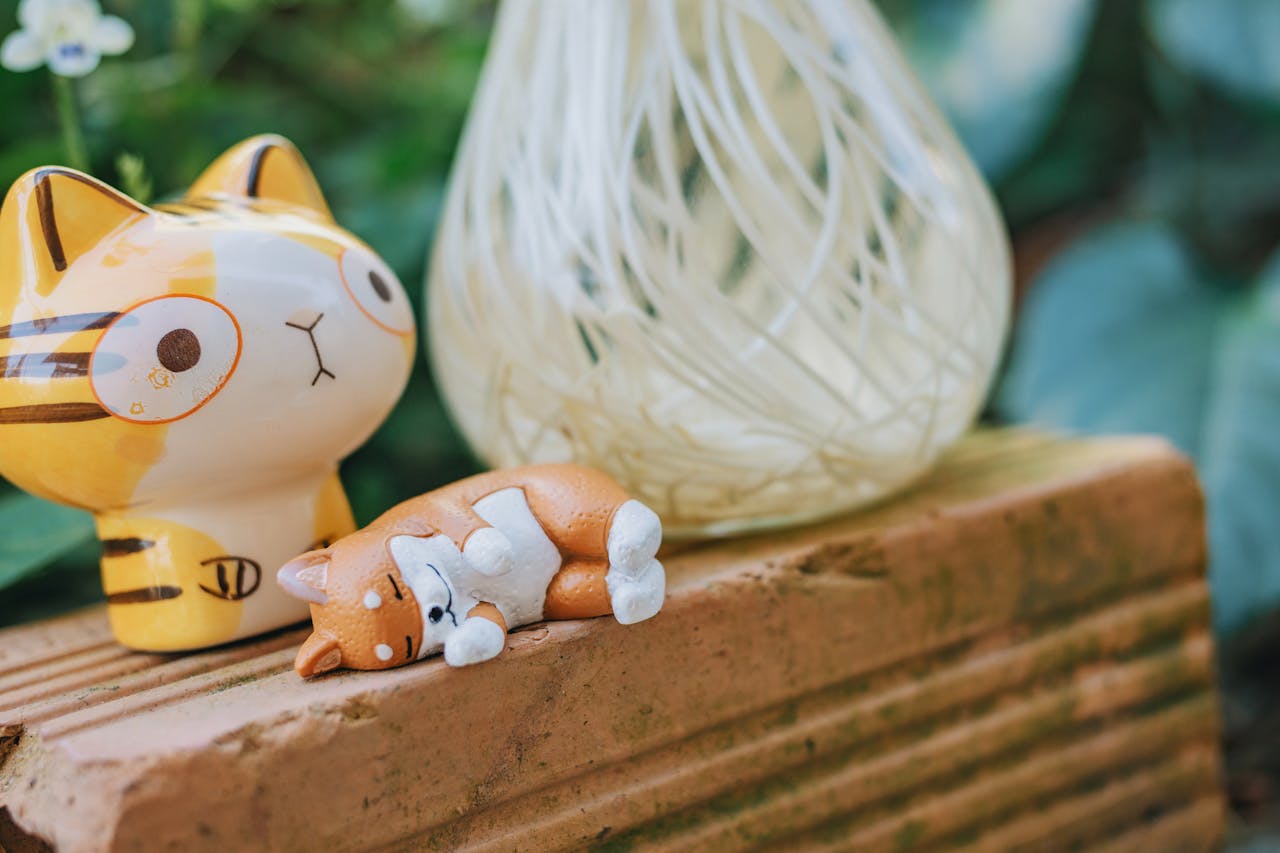 Adorable ceramic cat figurines placed on a rustic brick surface with a blurred green background.